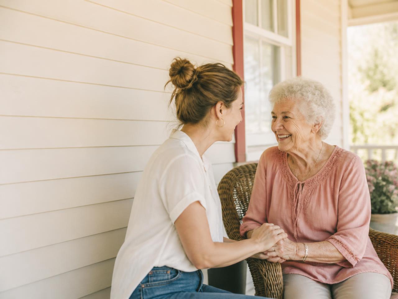 Acompanhante segurando as mãos de uma senhora sorridente na varanda
